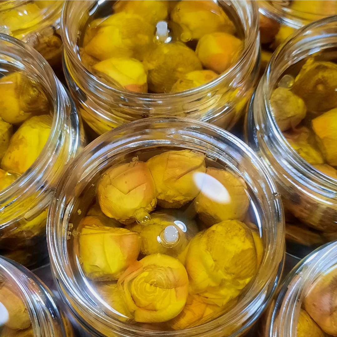 Vasetti di carciofini artigianali sott’olio in primo piano, immersi in olio extravergine d’oliva.